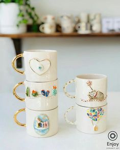 four coffee mugs are stacked on top of each other, with designs painted on them