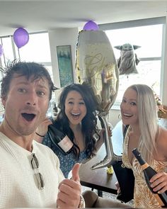 three people are posing for a photo with wine bottles in their hands and balloons behind them