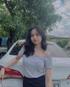 a woman standing next to a white car with her hand on the back of it