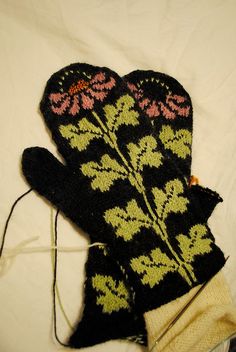 two black mittens with pink and green flowers on them sitting on a white sheet