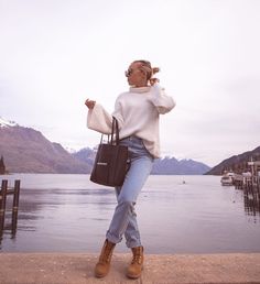 a woman standing on the edge of a pier with her hand in her hair and holding a purse