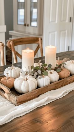 a wooden tray filled with white pumpkins and greenery on top of a table