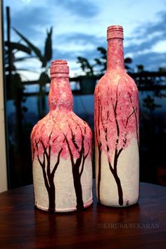 two bottles with trees painted on them sitting on a table