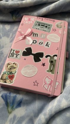 a pink notebook covered in stickers on top of a bed