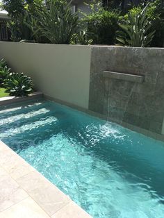 an outdoor swimming pool with water running down the side and trees in the back ground