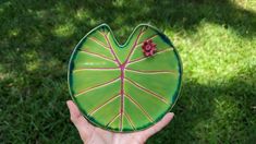 a hand holding a green leaf shaped plate with red flowers on it's center