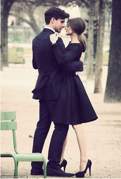 a man and woman standing next to each other in front of a green park bench