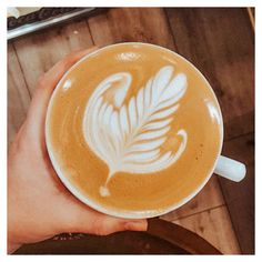 a person holding a cup of coffee on top of a wooden table