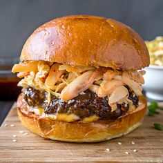 a sandwich with meat and cheese on a wooden cutting board next to a bowl of coleslaw