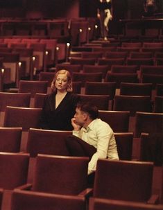 two people are sitting in the middle of an empty auditorium with rows of red seats