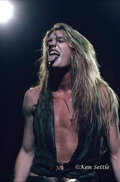 a man with long hair and no shirt on holding a microphone in his mouth while singing