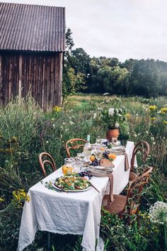 an outdoor table set for two with plates and glasses on it in the middle of a field