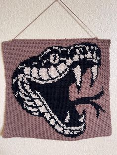 a crocheted wall hanging with an image of a snake on it's side