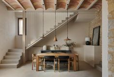 a dining room table and some chairs in a room with stone stairs leading up to the second floor