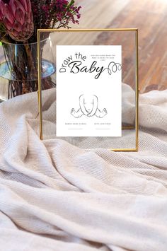 a baby shower sign sitting on top of a bed next to a vase filled with flowers