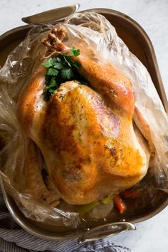 a roasted turkey in a roasting pan covered with plastic wrap and garnished with parsley