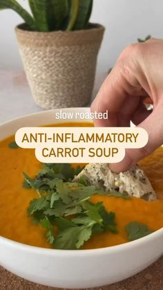 a person is dipping some food into a bowl with carrots and cilantro