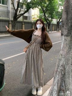 a woman wearing a mask standing next to a tree