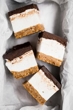 four pieces of cake sitting on top of white wax paper in a basket with some brown and white toppings