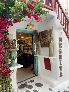 an entrance to a store with pink flowers on the wall and potted plants in front