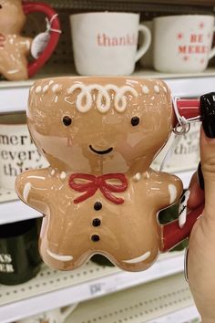 a person holding up a ceramic ginger ornament in front of shelves with coffee mugs