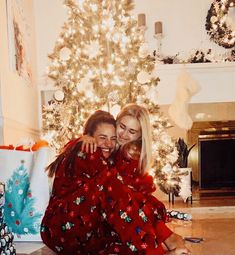 two women hugging each other in front of a christmas tree