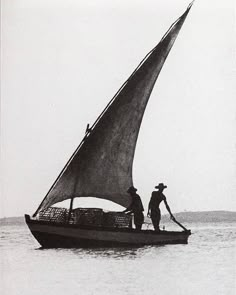 an old photo of two men on a sailboat in the water, with one man standing up