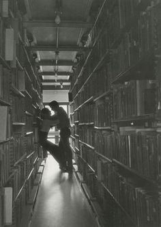 two people are kissing in the middle of a long aisle full of bookshelves