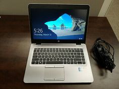 an open laptop computer sitting on top of a wooden desk next to a charger