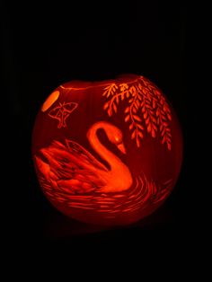 a pumpkin carved to look like a swan with leaves on its head and body, sitting in the dark