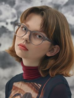 a young woman wearing glasses looking up at the sky with clouds in the back ground