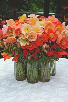 three vases filled with flowers sitting on top of a white tablecloth covered table