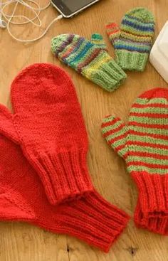 three knit mittens and gloves sitting on a table next to a laptop computer, mouse and headphones