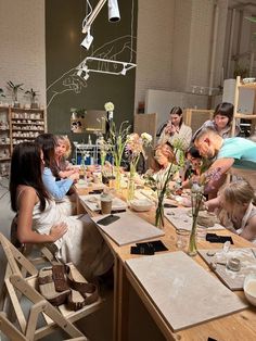 a group of people sitting around a table with flowers in vases and plates on it