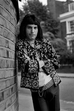 a black and white photo of a man leaning against a brick wall with his arms crossed