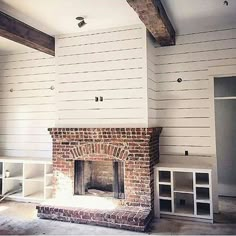 an empty living room with a brick fireplace and white shelving on either side of the fire place