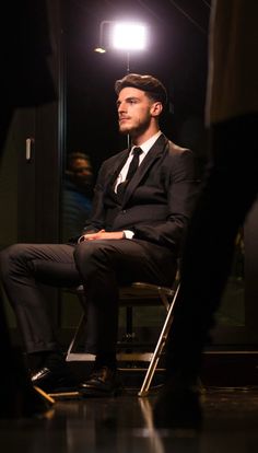 a man in a suit sitting on a chair with his legs crossed and head turned to the side