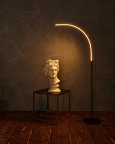 a white bust sitting on top of a wooden table next to a light that is turned on