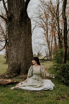 a woman sitting under a tree on top of a blanket in front of a large tree