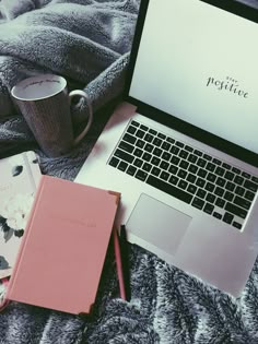 an open laptop computer sitting on top of a bed next to a cup of coffee