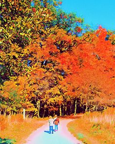 two people walking down a dirt road in the fall with trees turning orange and red