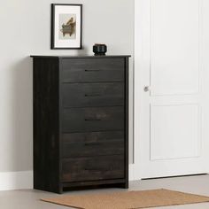 a black chest of drawers next to a white door with a brown rug on the floor