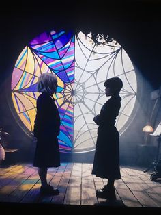 two people standing in front of a stained glass window on a wooden floor with lights coming from behind them