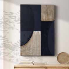 an abstract painting hangs on the wall above a wooden dresser with books and a basket