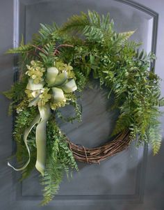 a wreath with green flowers and greenery hanging on a front door, ready to be hung