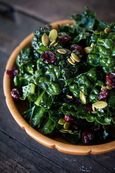 a bowl filled with greens and cranberries on top of a wooden table