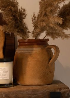 a brown vase sitting on top of a wooden shelf next to a candle and some feathers