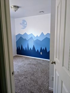 an empty room with blue mountains painted on the wall and carpeted flooring in front of it