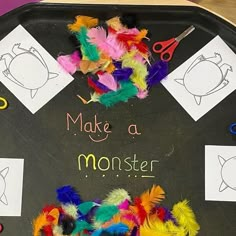 a black tray with colorful feathers and scissors on it that says, make a monster