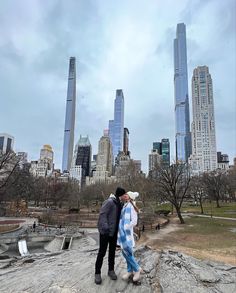 a man and woman standing on top of a rock in the middle of a park